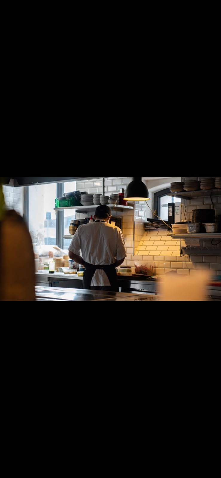 Una persona con delantal trabaja de espaldas en la cocina de un restaurante.